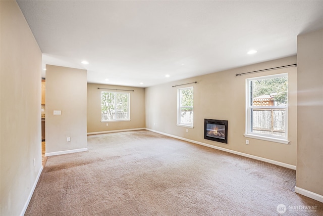 unfurnished living room featuring carpet flooring, baseboards, a glass covered fireplace, and recessed lighting