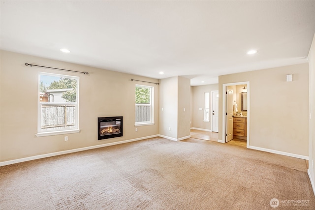 unfurnished living room with light carpet, recessed lighting, baseboards, and a glass covered fireplace