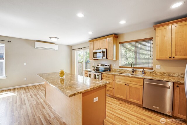 kitchen with appliances with stainless steel finishes, a sink, an AC wall unit, a kitchen island, and light wood finished floors