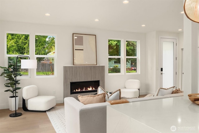 living area with light wood-type flooring, recessed lighting, baseboards, and a glass covered fireplace