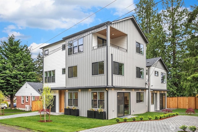 multi unit property featuring fence, a front lawn, board and batten siding, a balcony, and driveway