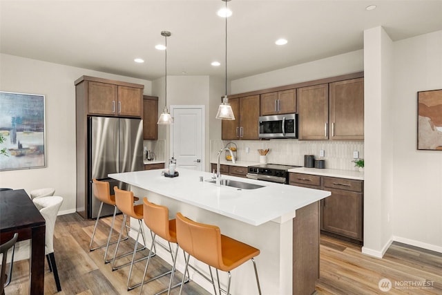 kitchen with baseboards, light wood-type flooring, tasteful backsplash, a sink, and stainless steel appliances
