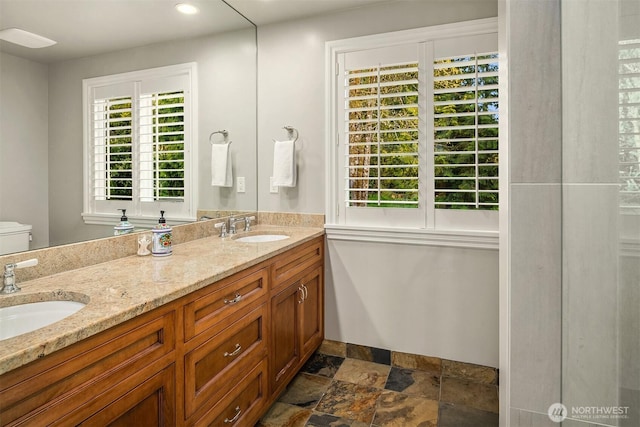 bathroom with double vanity, a sink, stone finish floor, and toilet