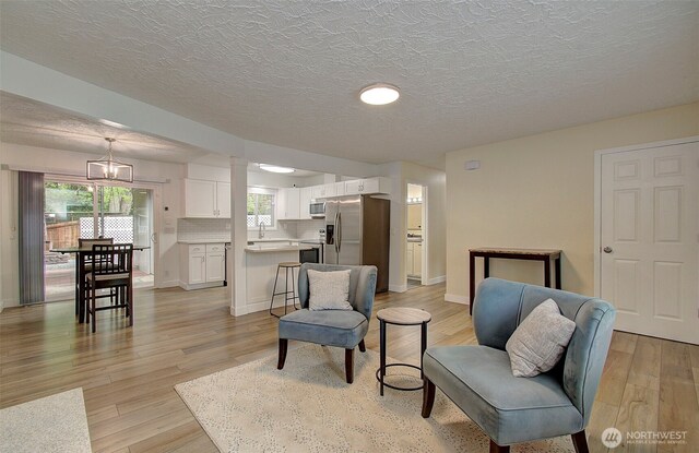 living area with baseboards, light wood-type flooring, and a textured ceiling