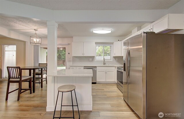 kitchen with backsplash, appliances with stainless steel finishes, light wood-type flooring, a sink, and white cabinets