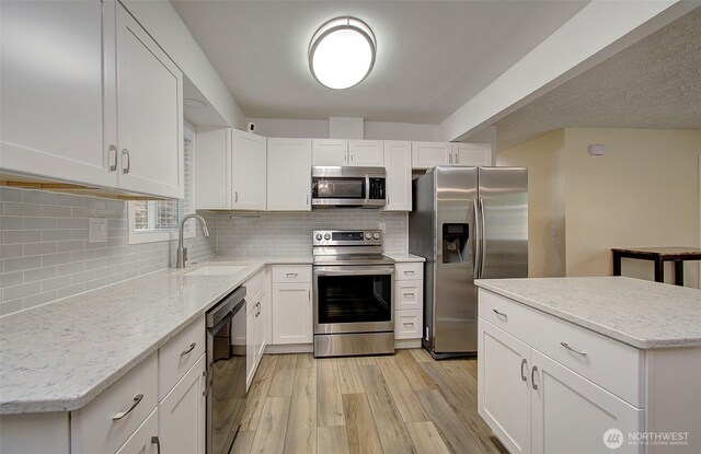 kitchen featuring white cabinetry, a sink, light wood-style flooring, backsplash, and stainless steel appliances