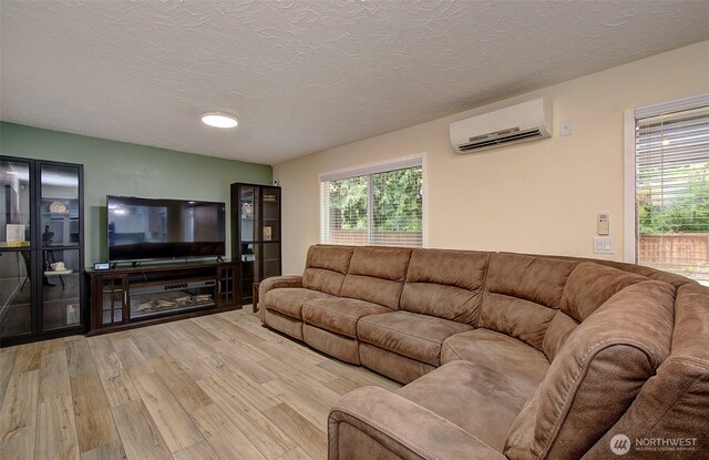 living room featuring a textured ceiling, light wood-style flooring, and a wall mounted air conditioner