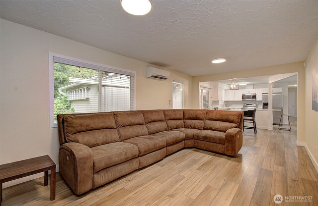 living area featuring a textured ceiling, baseboards, light wood-style flooring, and a wall mounted air conditioner