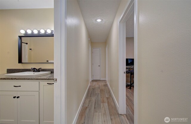 hallway with a sink, baseboards, light wood-type flooring, and a textured ceiling