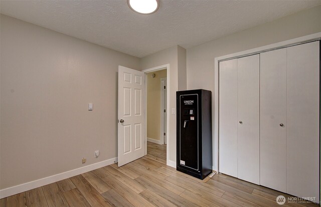 unfurnished bedroom with baseboards, a textured ceiling, light wood-style flooring, and a closet