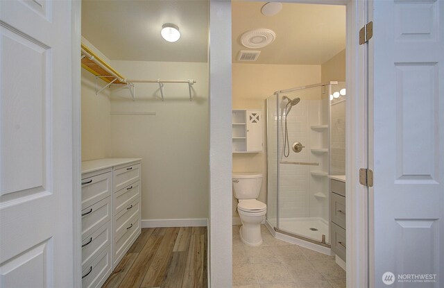 bathroom with a walk in closet, a shower stall, toilet, and visible vents