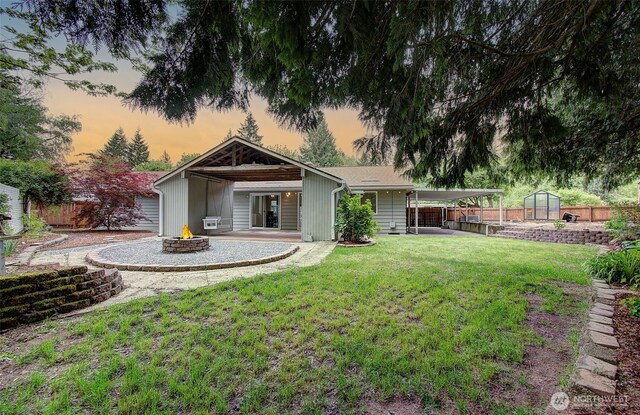 back of property at dusk featuring a patio area, a fire pit, fence, and a yard