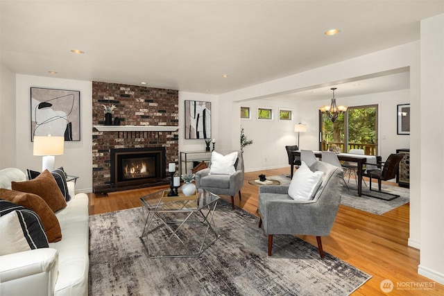 living area featuring a chandelier, light wood-type flooring, a brick fireplace, baseboards, and recessed lighting