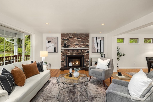 living area with wood finished floors, baseboards, recessed lighting, and a brick fireplace