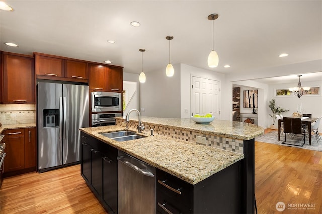 kitchen featuring appliances with stainless steel finishes, a sink, backsplash, light wood-style floors, and decorative light fixtures