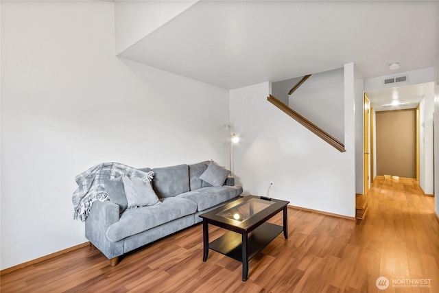 living room featuring baseboards, light wood-style floors, visible vents, and stairs