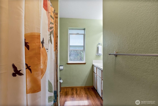 bathroom featuring baseboards, wood finished floors, a shower with shower curtain, a textured wall, and vanity