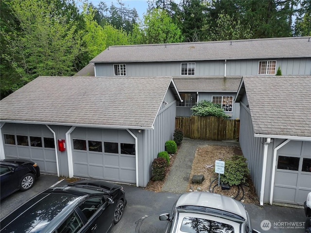 view of front facade featuring fence, aphalt driveway, roof with shingles, and a garage