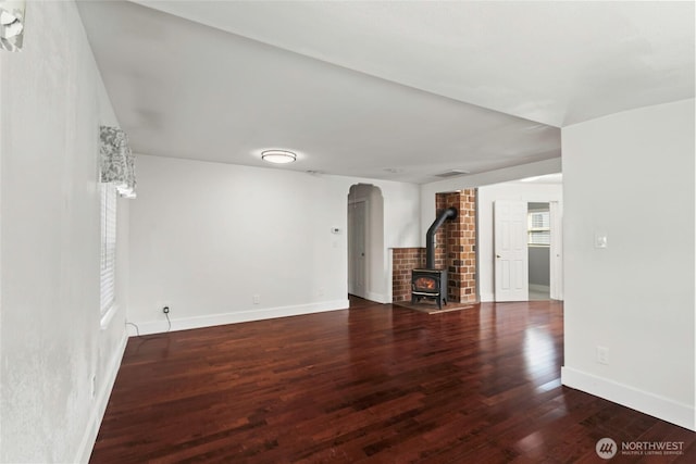 unfurnished living room featuring wood finished floors, arched walkways, a wood stove, baseboards, and visible vents