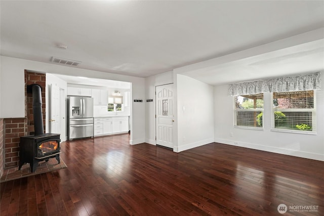 unfurnished living room featuring a wood stove, dark wood finished floors, visible vents, and baseboards