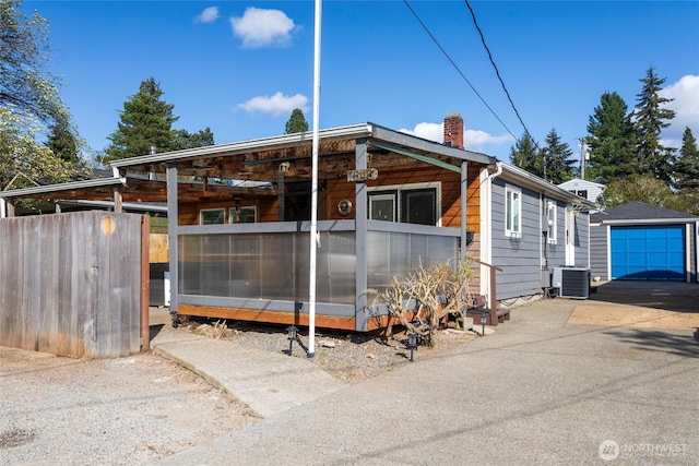 view of front facade with central air condition unit, a garage, an outdoor structure, a chimney, and concrete driveway