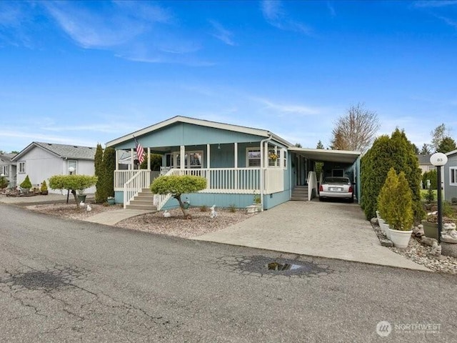manufactured / mobile home with concrete driveway, an attached carport, and a porch