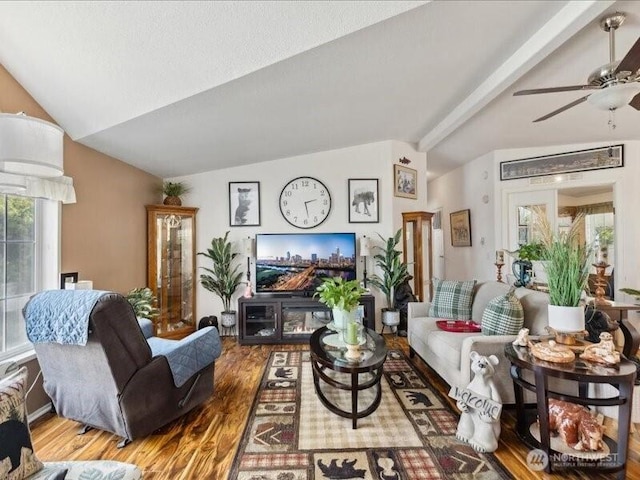 living area with wood finished floors, vaulted ceiling with beams, and a ceiling fan