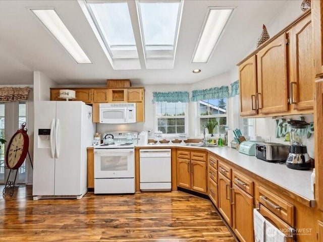 kitchen with a sink, dark wood finished floors, a skylight, white appliances, and light countertops