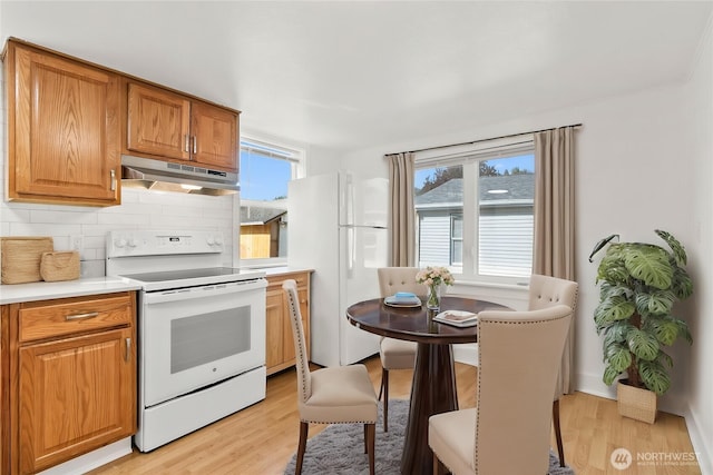kitchen with decorative backsplash, light countertops, light wood finished floors, under cabinet range hood, and white appliances