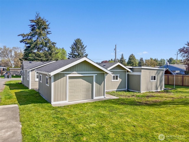 rear view of property featuring a garage, fence, a yard, and a shingled roof