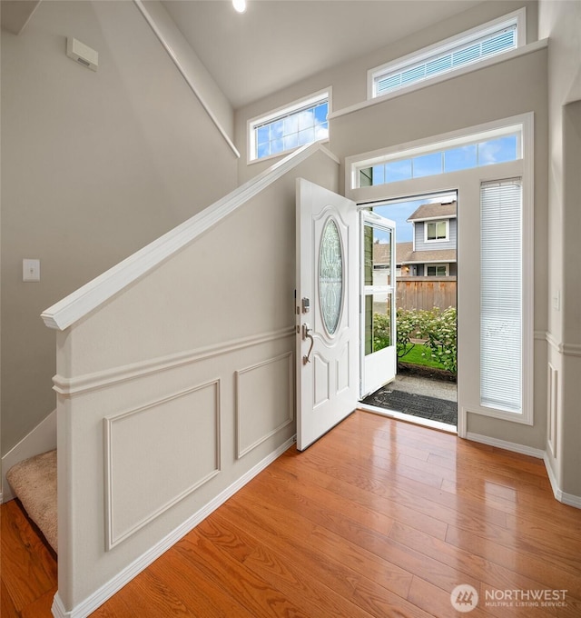 foyer featuring a decorative wall, wood finished floors, stairway, and a wainscoted wall