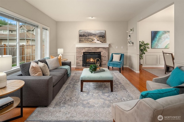 living room with wainscoting, a decorative wall, a brick fireplace, and wood finished floors