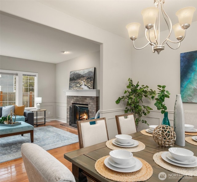 dining space featuring a brick fireplace, a wainscoted wall, light wood finished floors, a chandelier, and a decorative wall