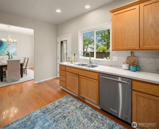 kitchen featuring stainless steel dishwasher, decorative backsplash, an inviting chandelier, a sink, and light wood-style flooring