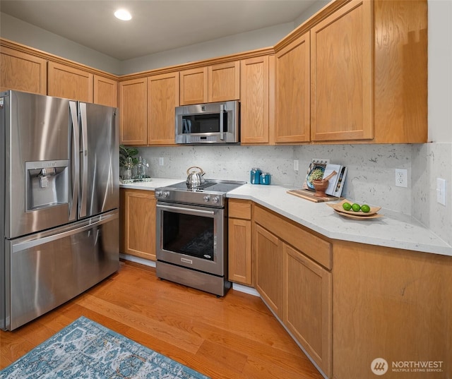 kitchen with appliances with stainless steel finishes, decorative backsplash, light stone counters, and light wood-style floors