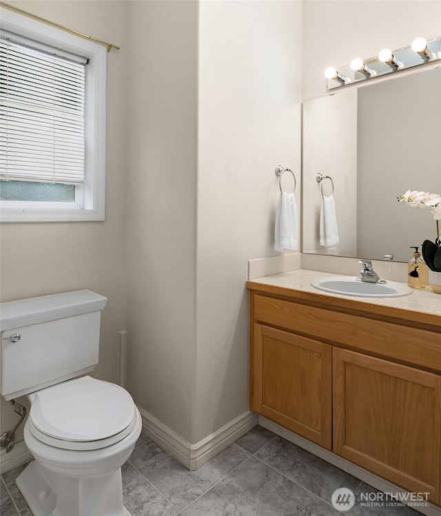 half bathroom featuring vanity, baseboards, and toilet