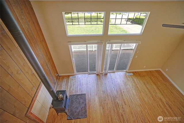 366 Tillicum Way, Camano Island, WA 98282 - unfurnished living room featuring baseboards, visible vents, wood finished floors, a wood stove, and a high ceiling