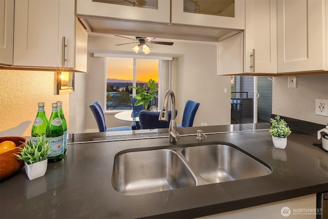 kitchen featuring white cabinets, a sink, dark countertops, ceiling fan, and a peninsula