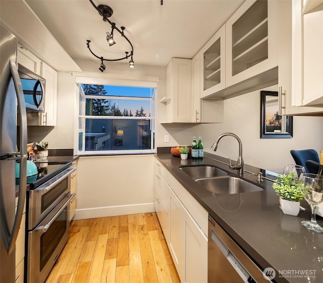 kitchen with light wood-style flooring, appliances with stainless steel finishes, dark countertops, a sink, and white cabinetry