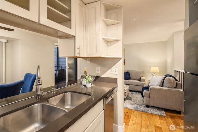 kitchen with open shelves, light wood-style floors, appliances with stainless steel finishes, dark countertops, and a sink
