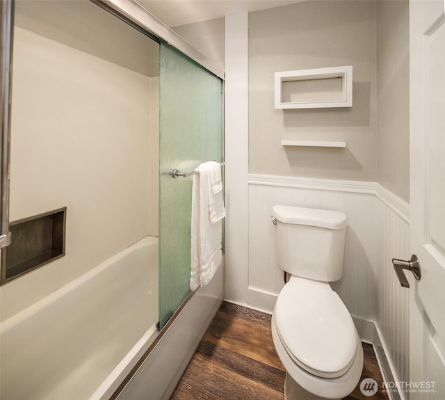 bathroom with enclosed tub / shower combo, wood finished floors, a wainscoted wall, and toilet