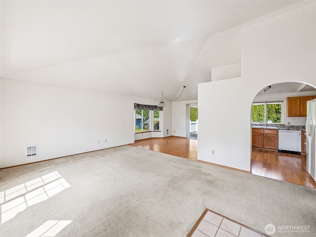 unfurnished living room featuring visible vents, light colored carpet, arched walkways, high vaulted ceiling, and an inviting chandelier