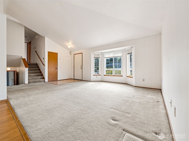 unfurnished living room featuring wood finished floors, baseboards, high vaulted ceiling, stairway, and carpet