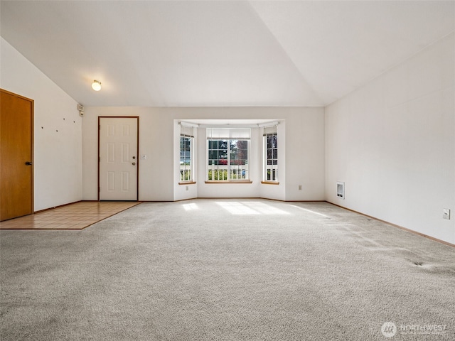 spare room with carpet floors, baseboards, vaulted ceiling, and visible vents
