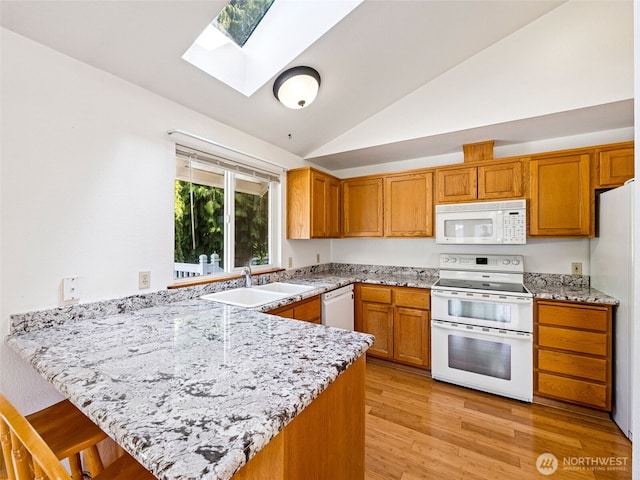 kitchen with a peninsula, white appliances, a breakfast bar, lofted ceiling with skylight, and a sink