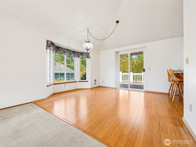 unfurnished dining area featuring baseboards, light wood-style flooring, lofted ceiling, and a chandelier