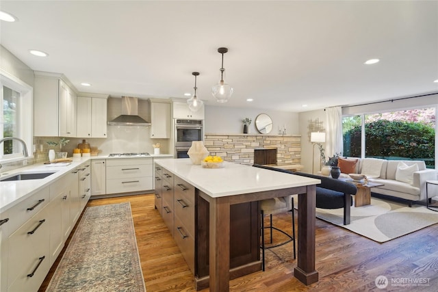 kitchen with light wood-type flooring, a sink, recessed lighting, and wall chimney range hood