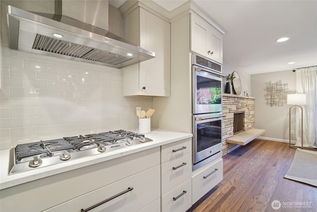 kitchen with wall chimney range hood, tasteful backsplash, light countertops, baseboards, and stainless steel appliances