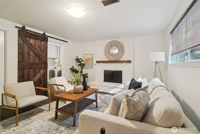 living area featuring visible vents, a brick fireplace, wood finished floors, a barn door, and washer and dryer