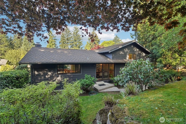 back of property with a lawn, a shingled roof, and a chimney